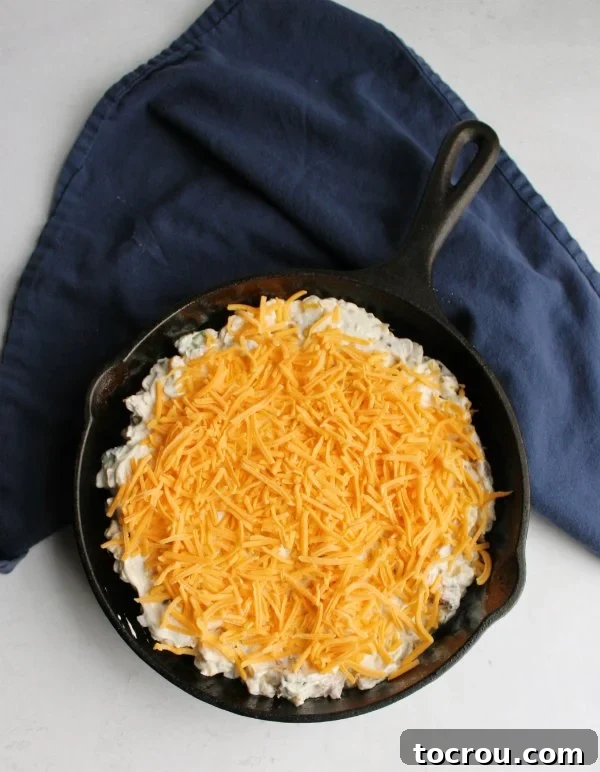 Ultimate Creamy Pulled Pork Dip 3 A cast iron skillet filled with delicious pulled pork dip, generously topped with shredded cheddar cheese and ready to be baked in the oven.