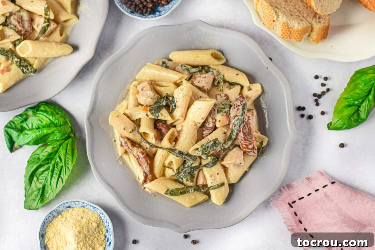 Plate of creamy Tuscan chicken pasta featuring penne, spinach, chicken, and sun-dried tomatoes in a luscious sauce.