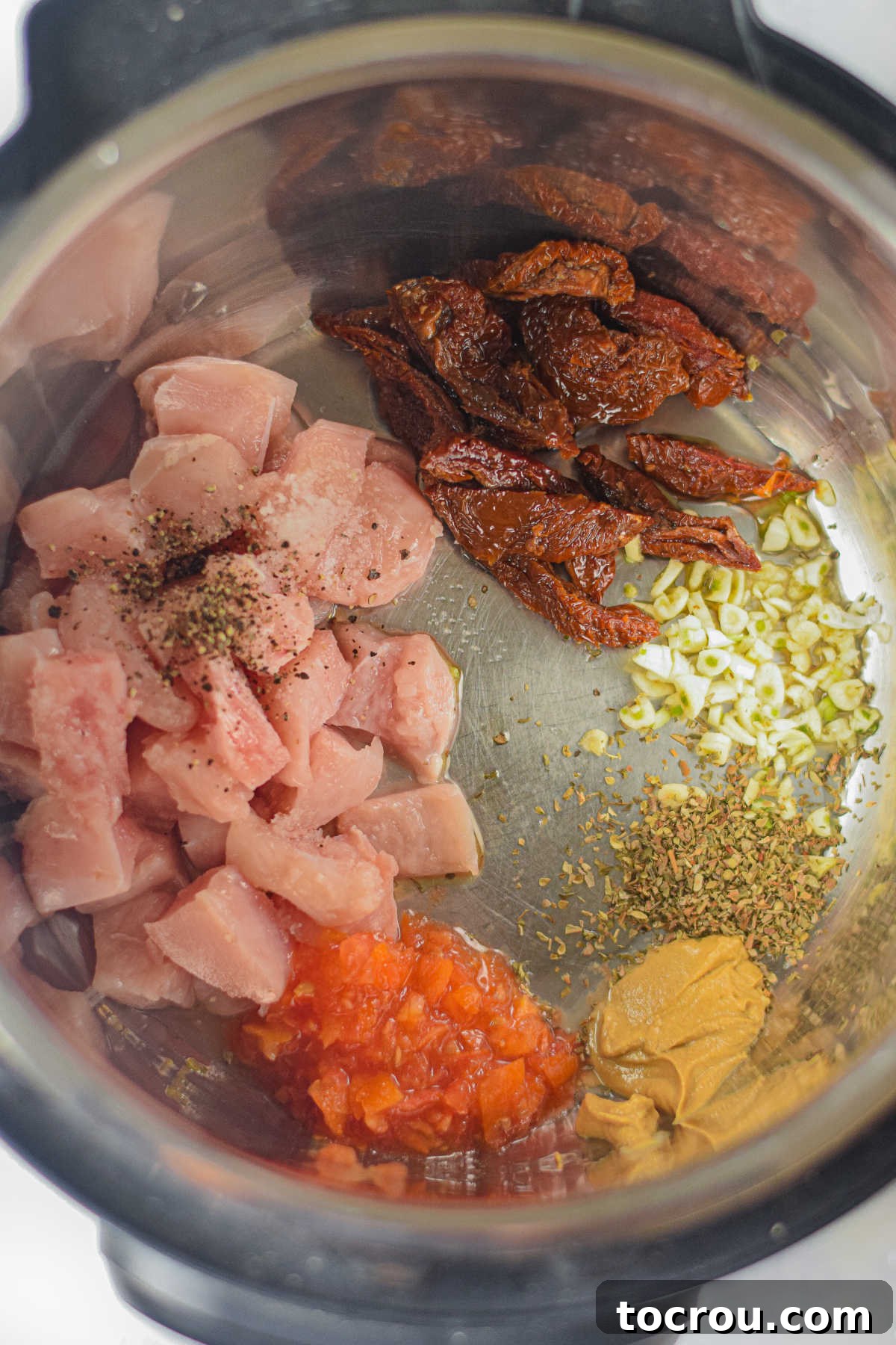 Cubed chicken, sun-dried tomatoes, minced garlic, Dijon mustard, and Italian seasonings mixed in the Instant Pot before cooking.