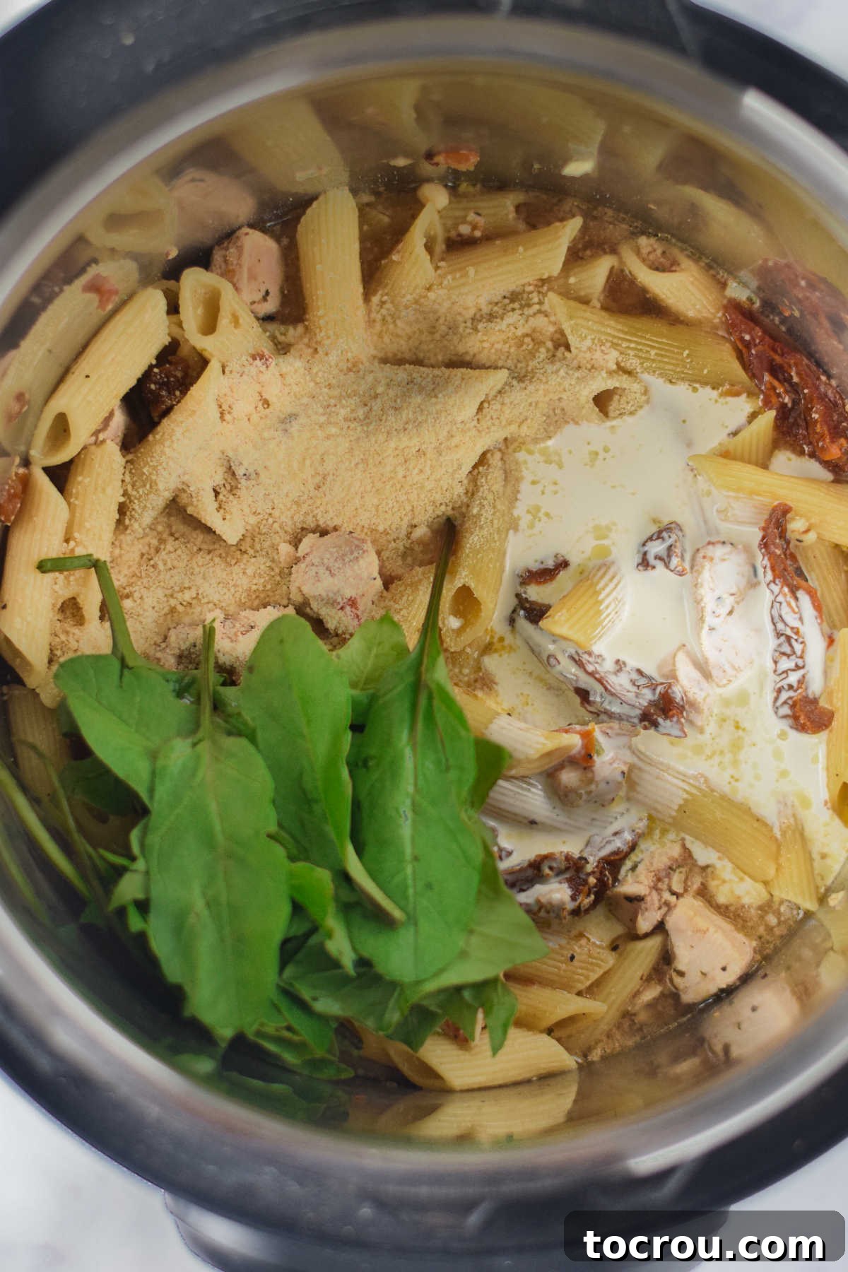 Adding heavy cream, grated Parmesan cheese, and fresh baby spinach to the cooked chicken and pasta mixture in the Instant Pot.