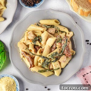 Plate of Tuscan chicken pasta with penne pasta, spinach, chicken and sun-dried tomatoes in creamy sauce.