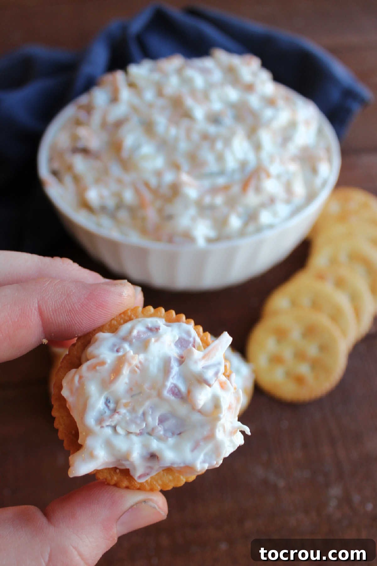 Hand holding a Ritz cracker generously topped with cheesy dill pickle dip
