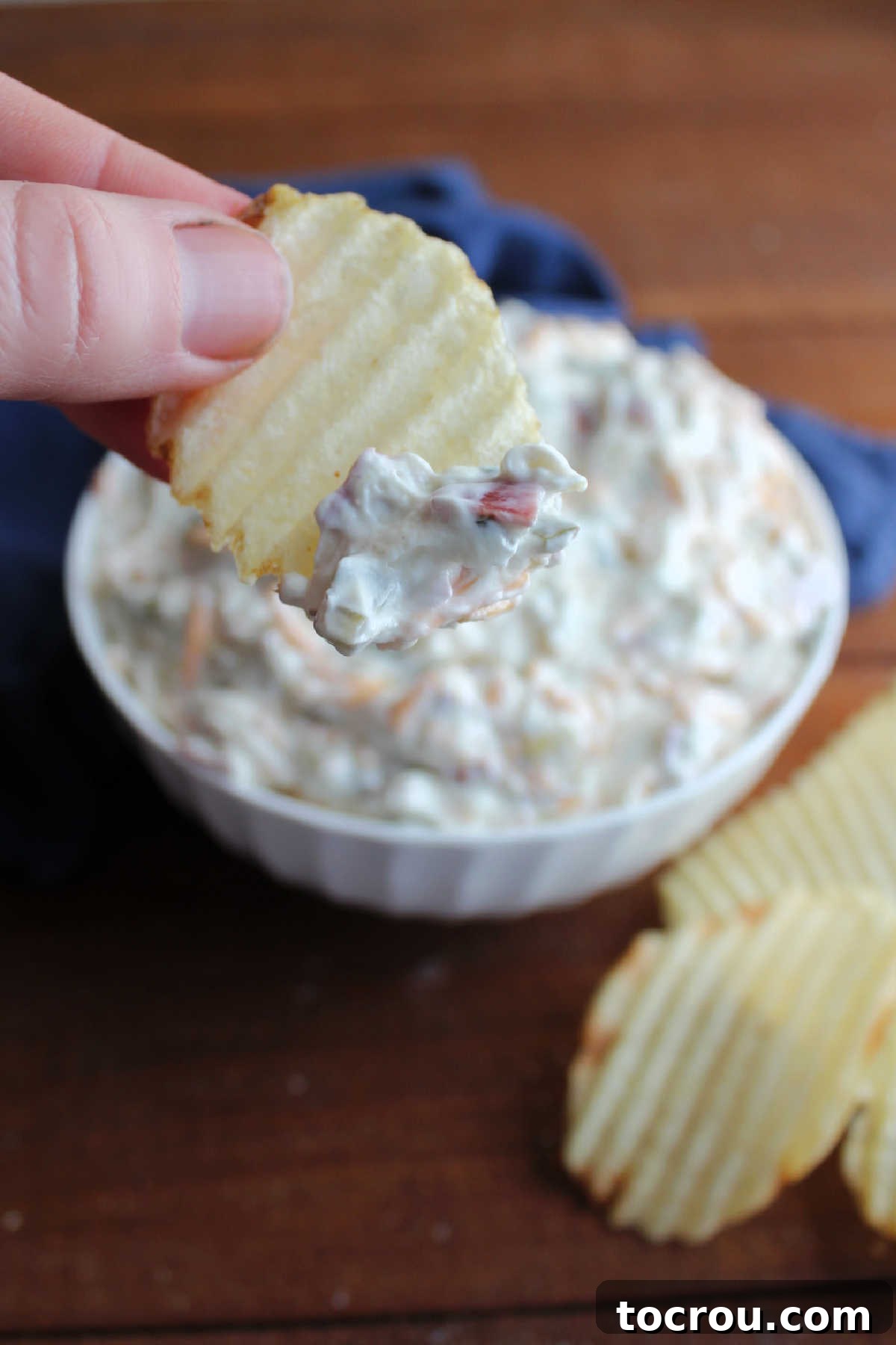 Ruffled potato chip being dipped into a bowl of creamy dill pickle wrap dip, showing its thick texture