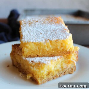 Stack of lemon gooey butter cake bars with cakey crust and gooey cream cheese, lemon and butter topping.