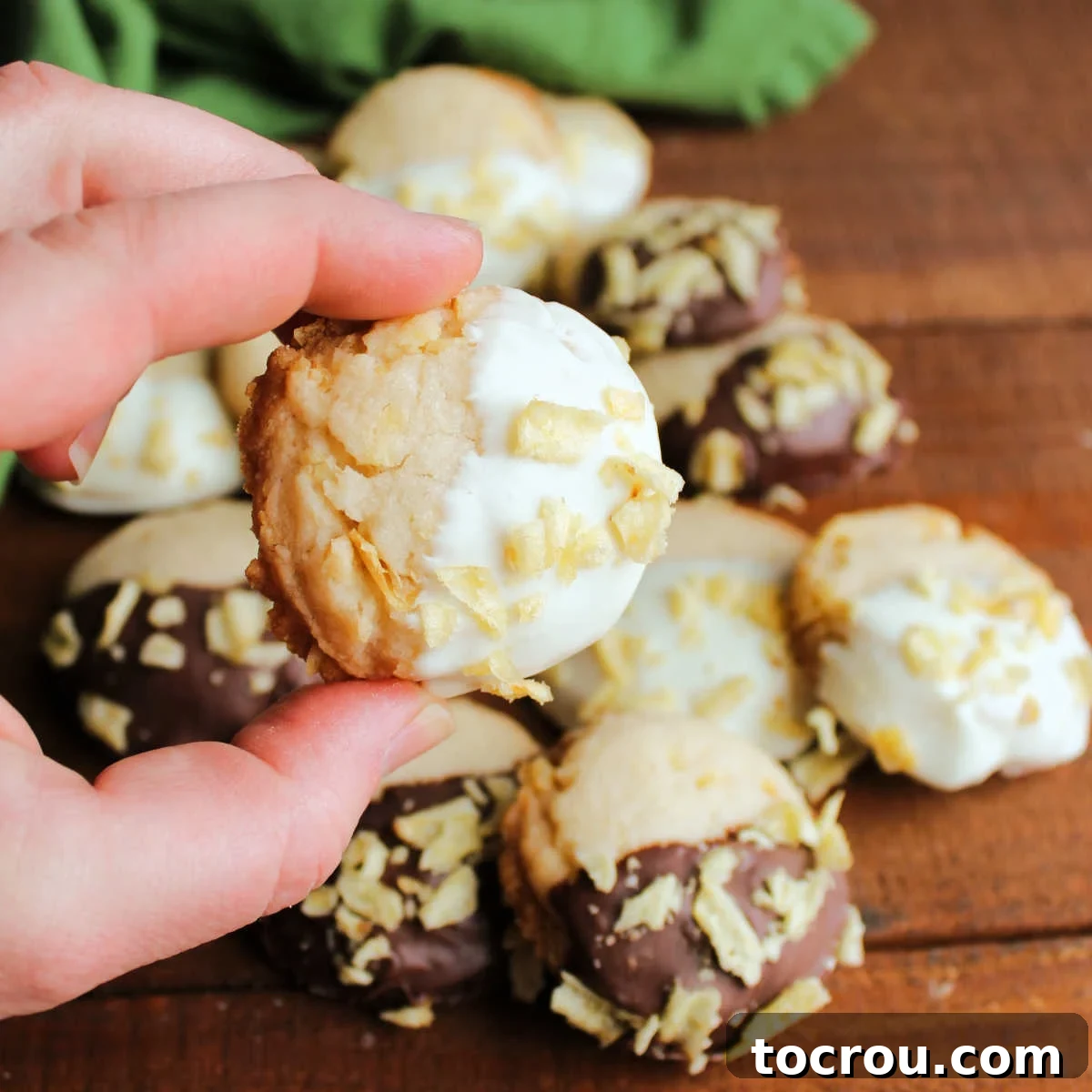 Grandmas Golden Crunch Cookies 2 Hand holding potato chip shortbread cookie with half of the cookie coated in white chocolate and sprinkled with bits of potato chips.