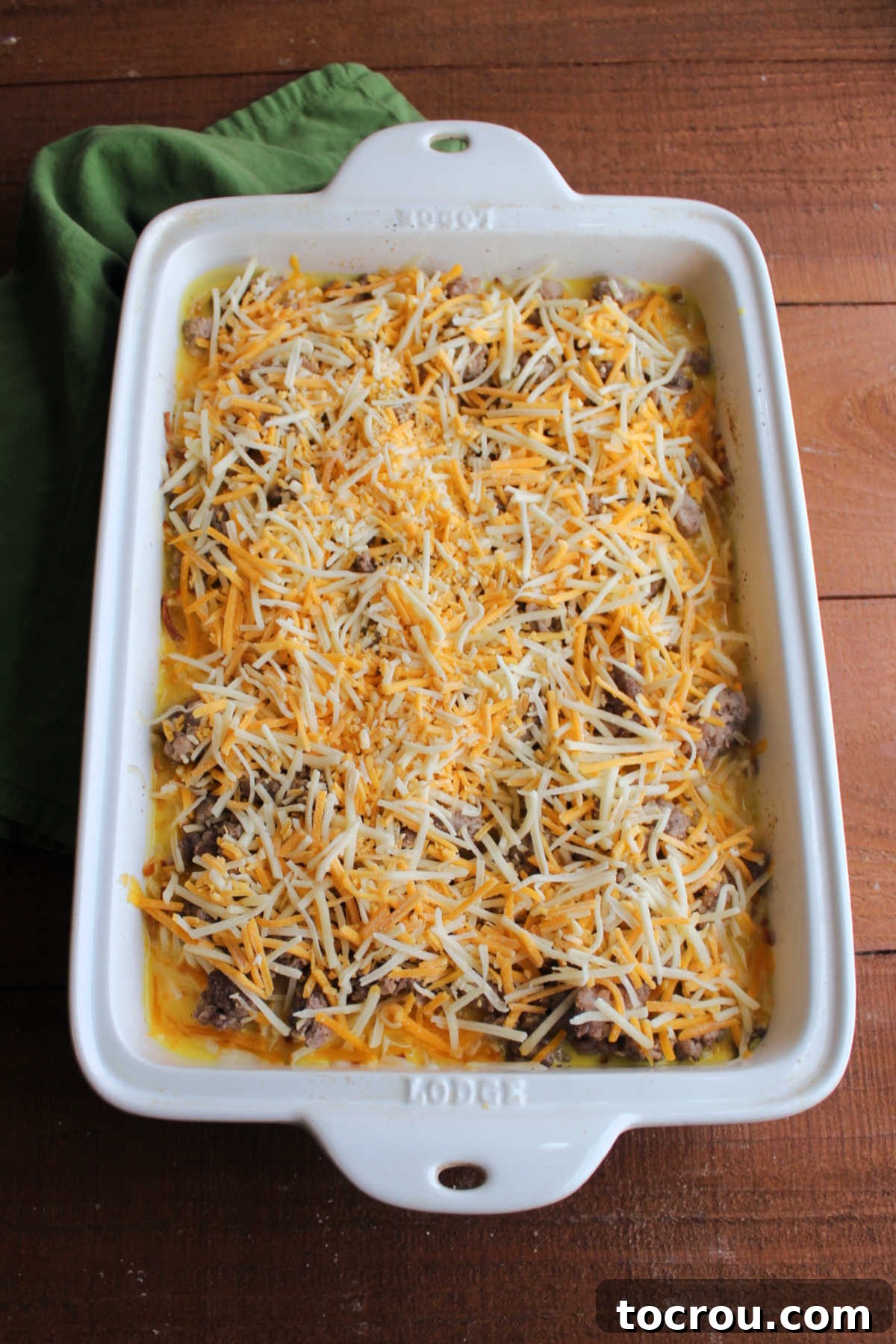Casserole Ready for Baking An unbaked sausage, egg, and hashbrown casserole generously topped with shredded cheese, ready to be placed into the oven.