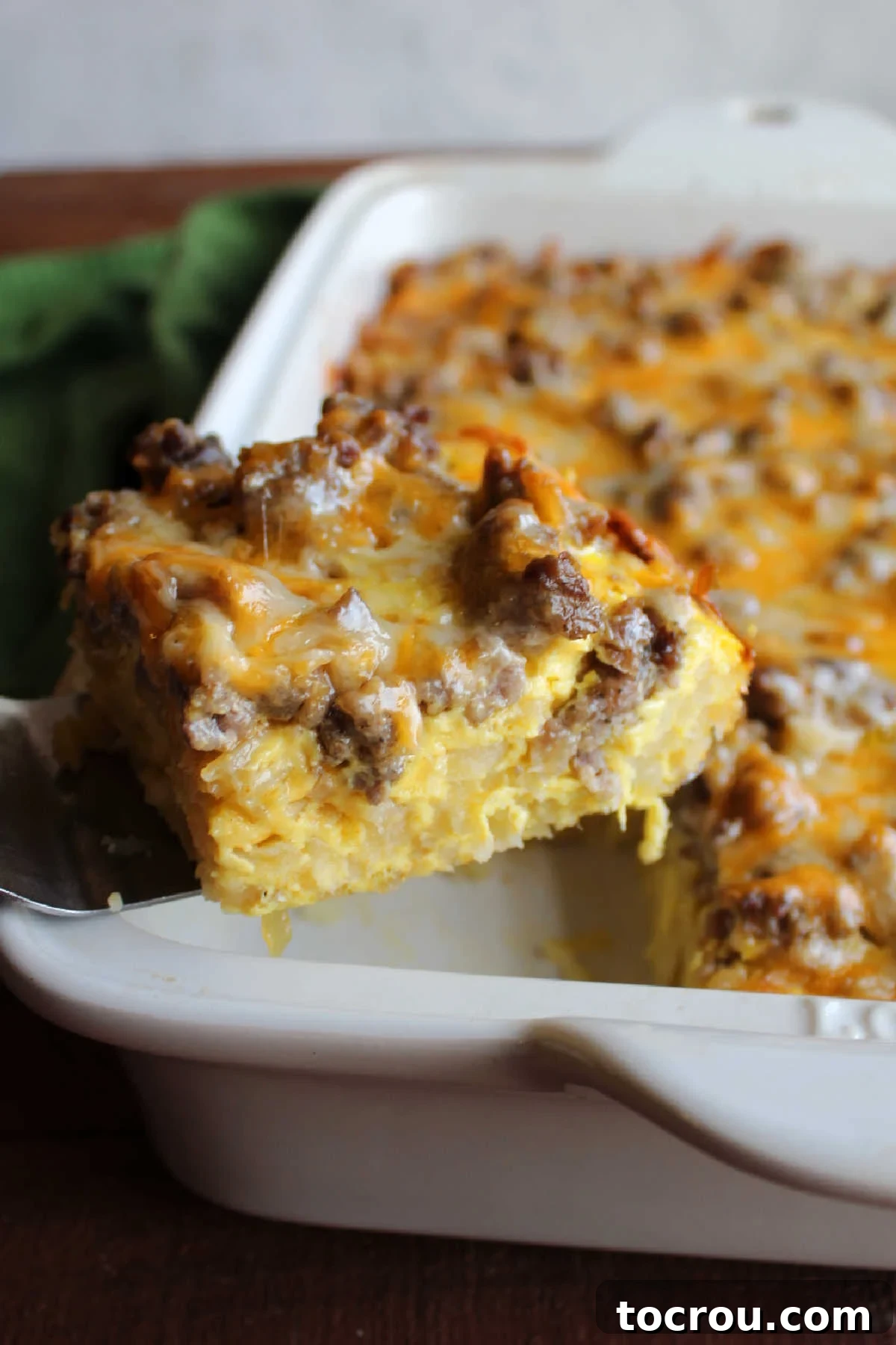 Serving a Piece of Casserole A serving of sausage hashbrown egg casserole being lifted from the baking pan with a spatula, showcasing its fluffy texture and golden-brown crust.
