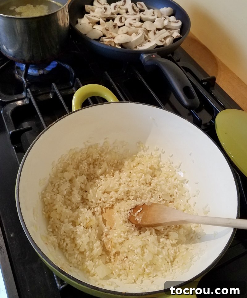Risotto in Progress Enameled cast iron saucier with partially cooked rice and a wooden spoon, with a skillet of sliced mushrooms in the background, illustrating the risotto cooking process.