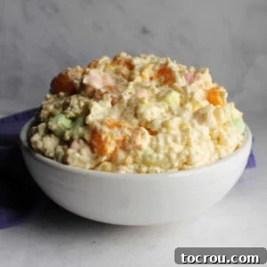 white serving bowl piled high with frog eye salad with bit of orange, pastel marshmallows, and pasta in a creamy custard mixture.