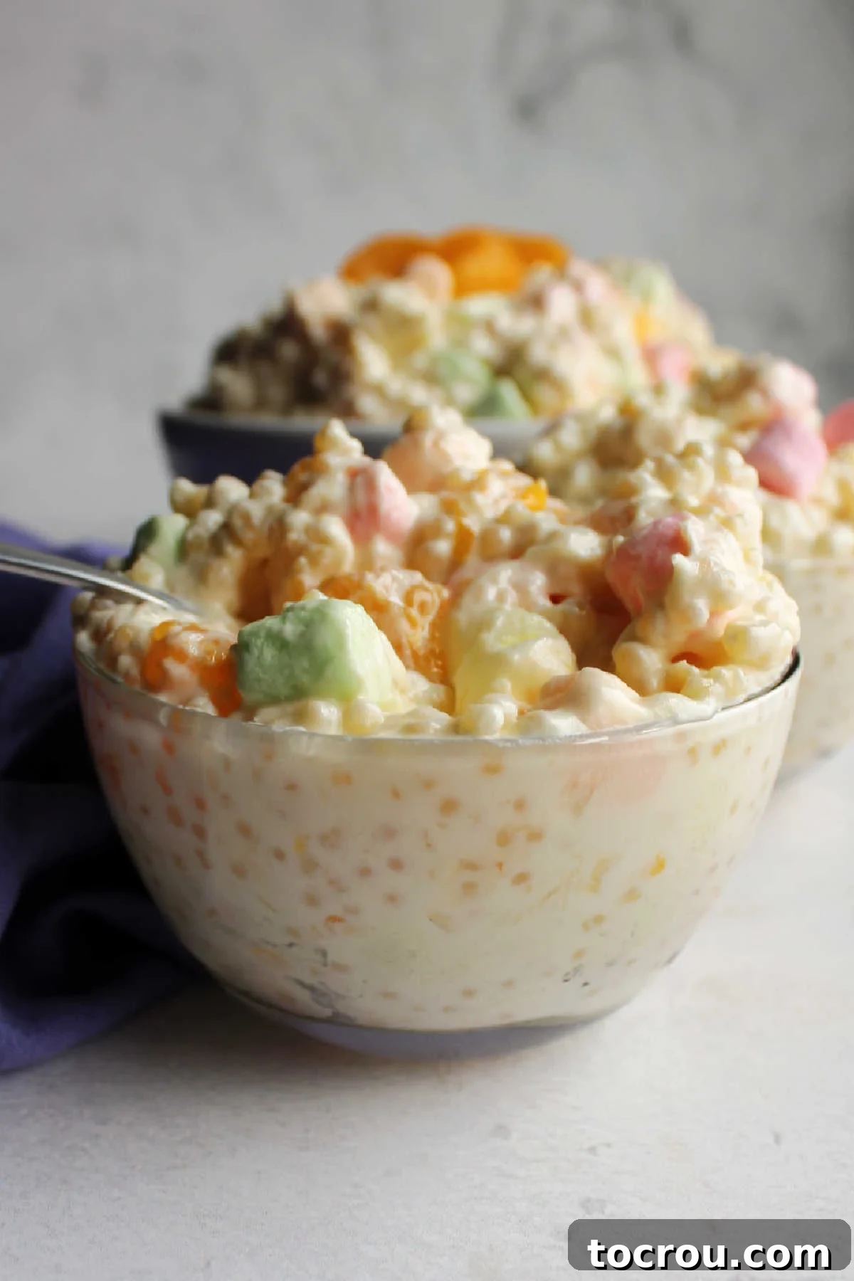Side view of a small glass bowl filled with frog eye salad showing the texture of the pasta through the glass bowl.