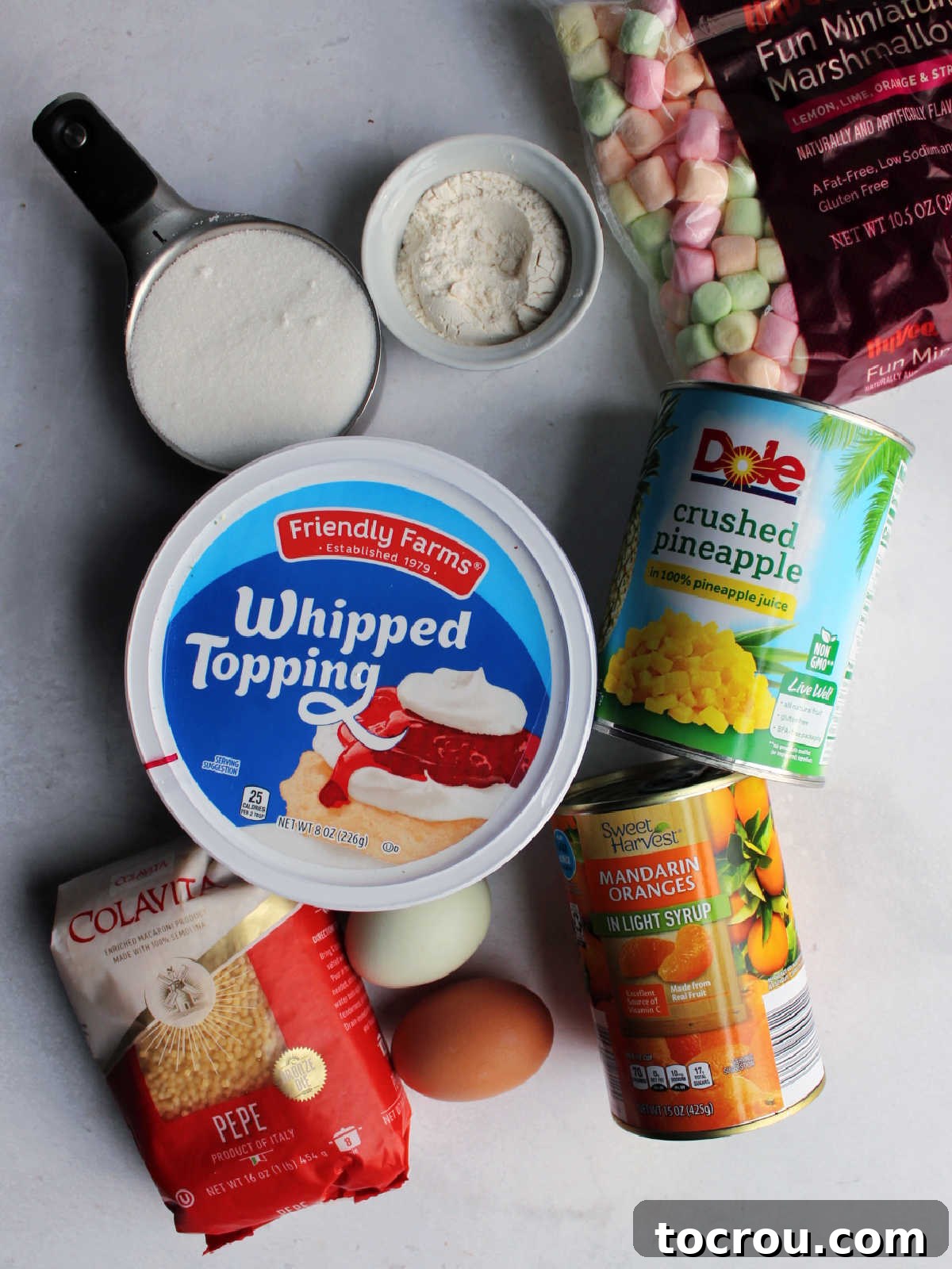 Ingredients including pepe pasta, eggs, crushed pineapple, sugar, flour, pastel marshmallows and a can of mandarin oranges ready to be made into easter frog egg salad.