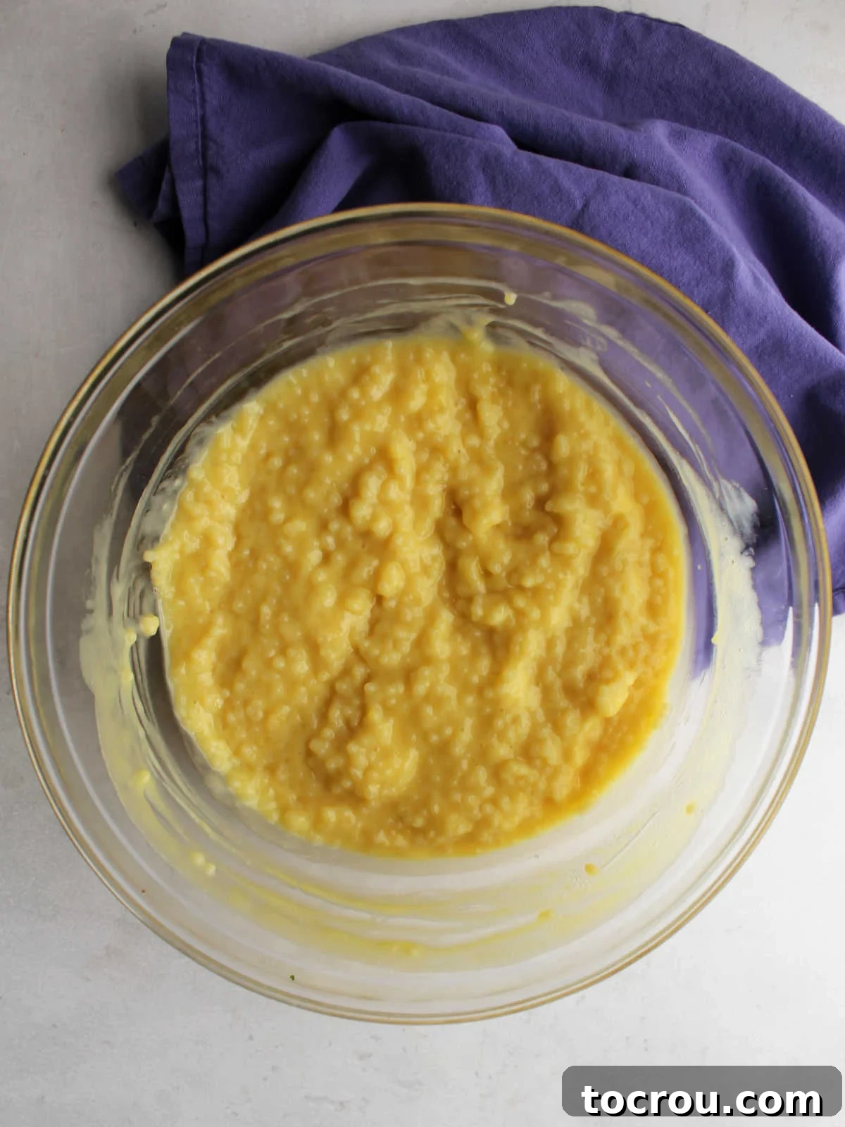 Glass mixing bowl filled with pasta mixed with custard mixture, ready to chill.