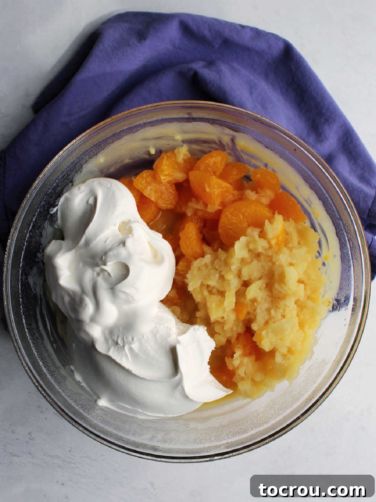 Crushed pineapple, mandarin oranges and whipped topping ready to be stirred into custard and pasta mixture.