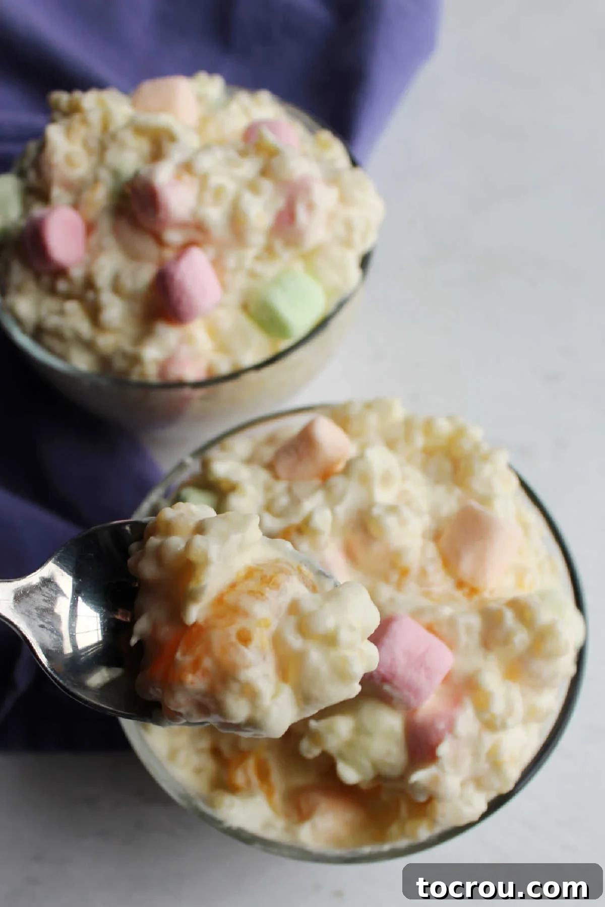 Spoonful of frog eye salad with piece of mandarin orange and small little pearls of pasta in a creamy fluffy pudding mixture.