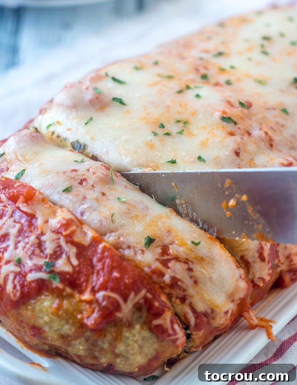 Slicing Chicken Parm Meatloaf Knife slicing chicken meatloaf topped with marinara and melted mozzarella cheese, about to show the melted cheese and pesto inside.
