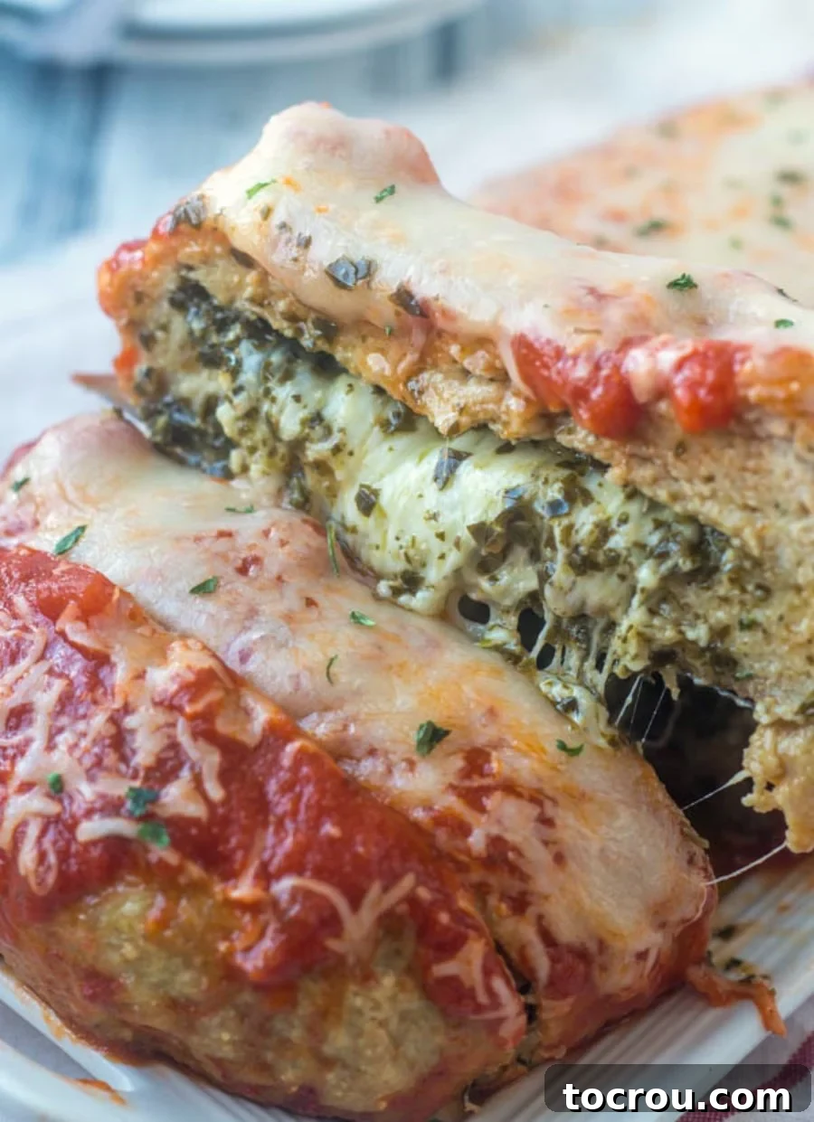Chicken Parmesan Meatloaf with Pesto Lifting slice of chicken parmesan meatloaf out of the loaf showing the melted cheese center with bits of pesto mixed in.