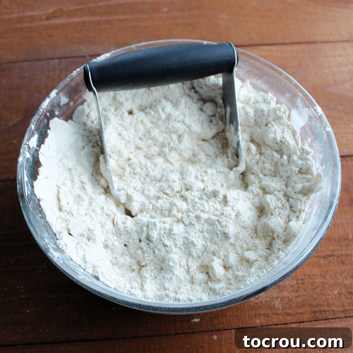 Cutting Lard into Flour with Pastry Cutter Mixing bowl of flour with lard cut into it with a pastry cutter, showing crumbly texture.