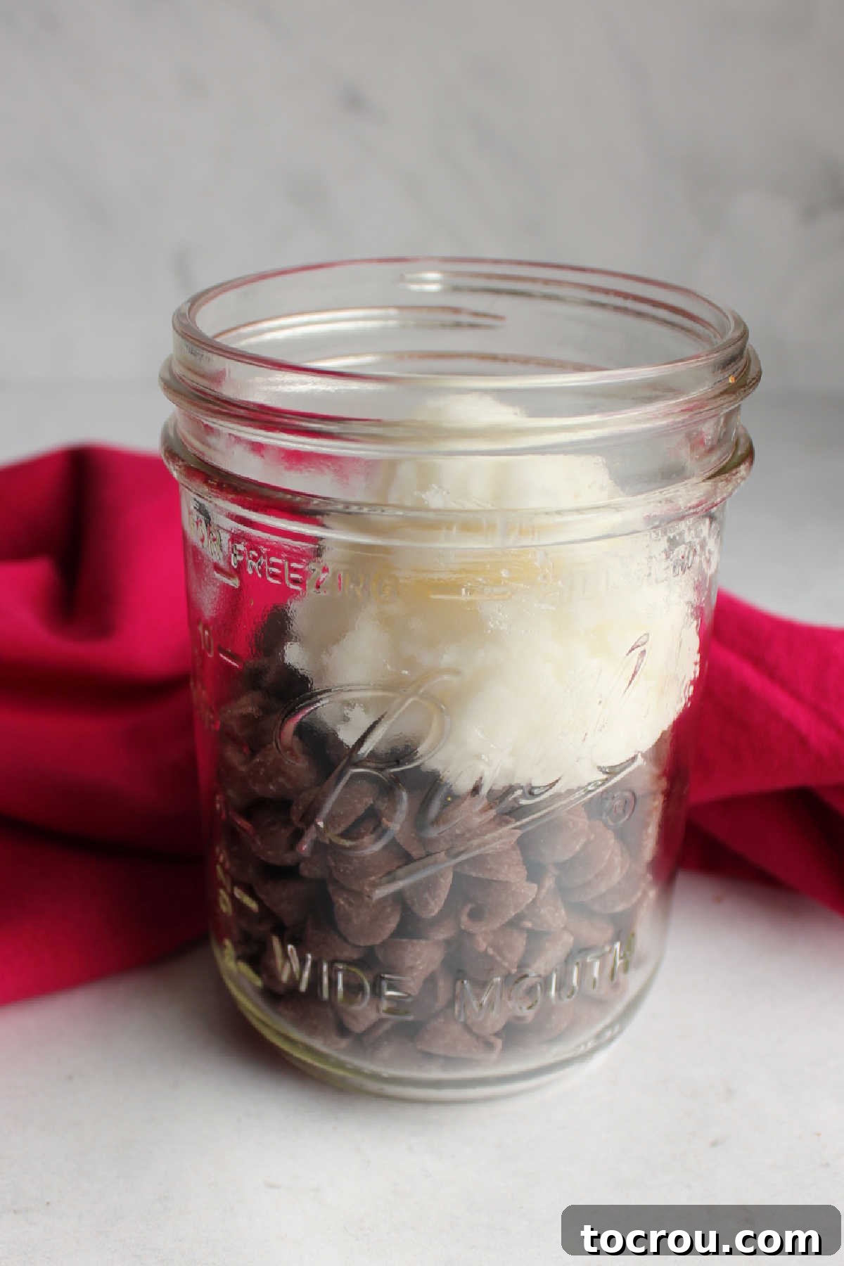 Ingredients in Jar for Melting Chocolate chips and solid coconut oil in a glass jar, ready to be melted for magic shell.