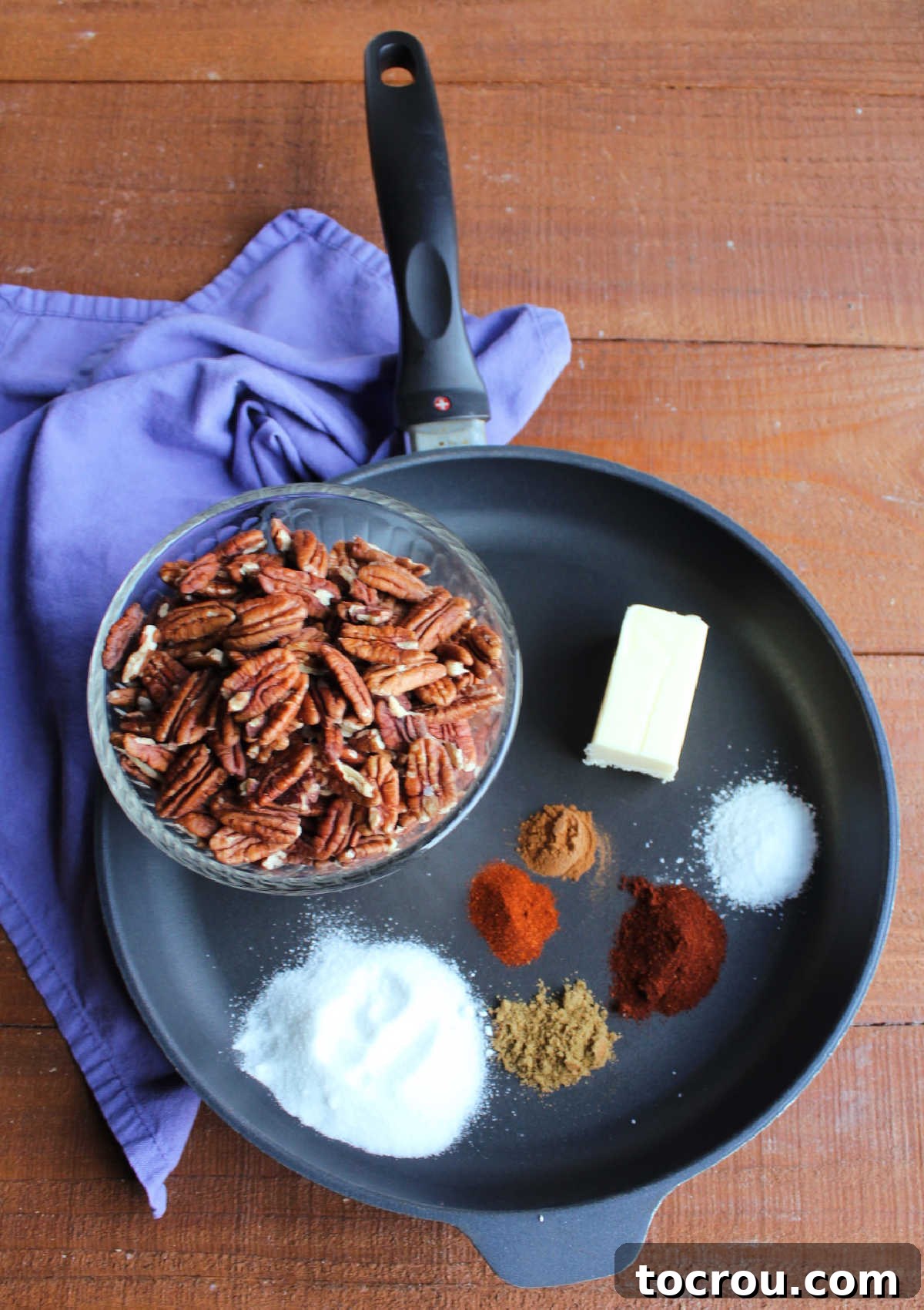 Spiced Pecan Ingredients Ingredients for spiced pecans in a skillet, including a bowl of pecans, butter, sugar, salt, and various seasonings.