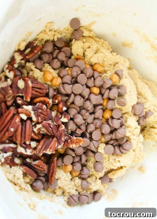 A bowl of rich cookie dough, generously studded with glistening chocolate chips, soft caramel bits, and chopped pecans, ready to be scooped and baked into delicious Turtle Cookies.