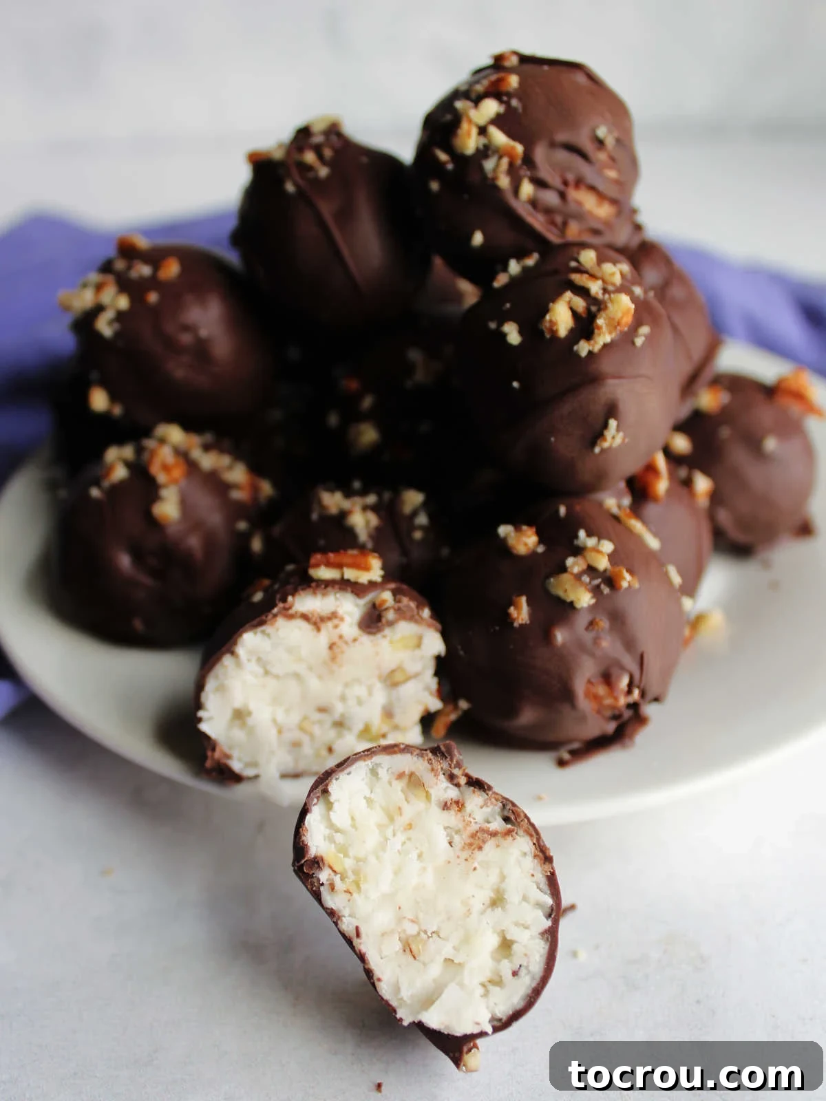 Pile of coconut bon bons topped with pecans in background with a bon bon cut in half in the front, showing the white filling.