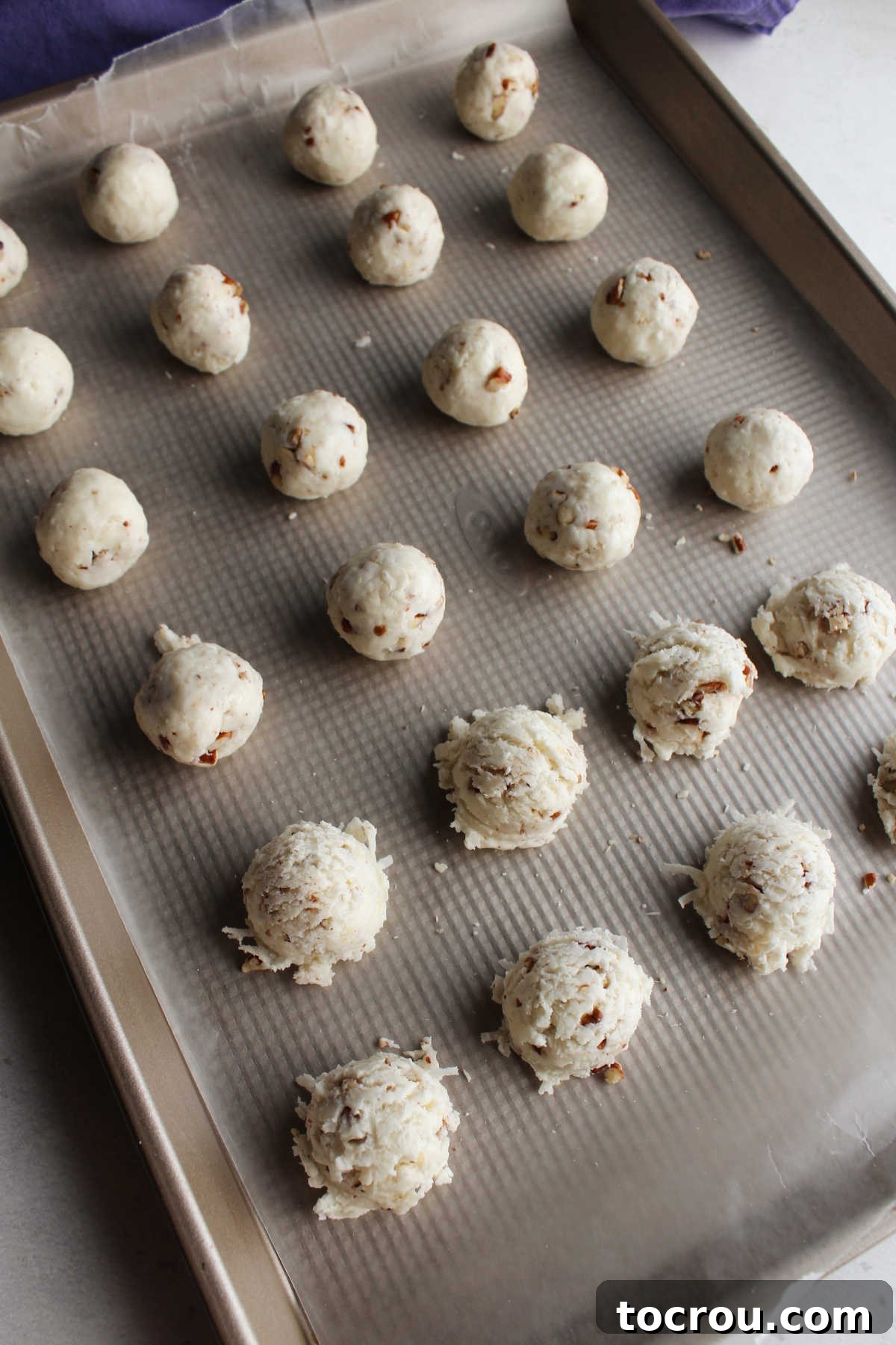 Tray of coconut bon bon centers, half just scooped and kind of jagged and half smoothed out after being rolled between palms.