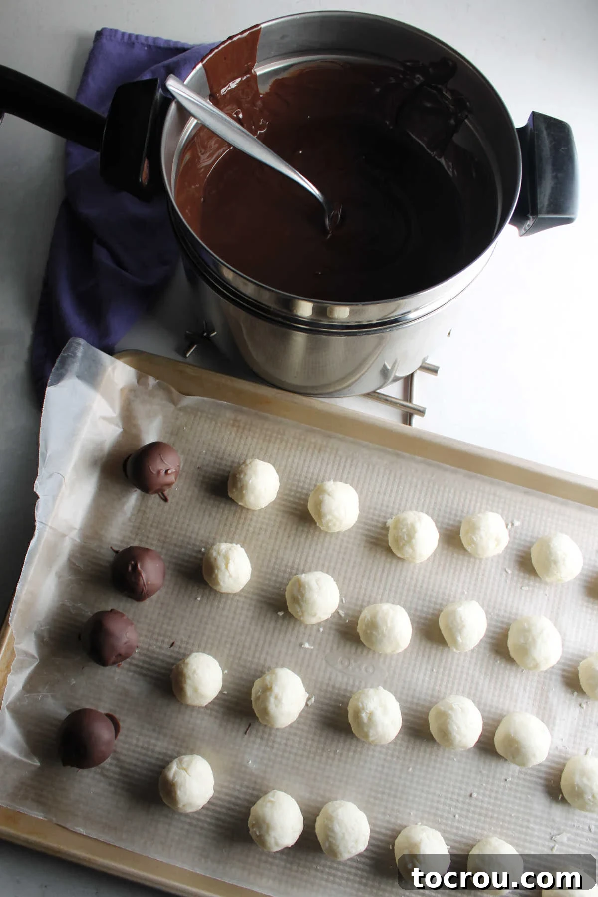 Double boiler of melted chocolate next to tray of chilled bon bon centers, some already dipped in chocolate and setting up on wax paper.