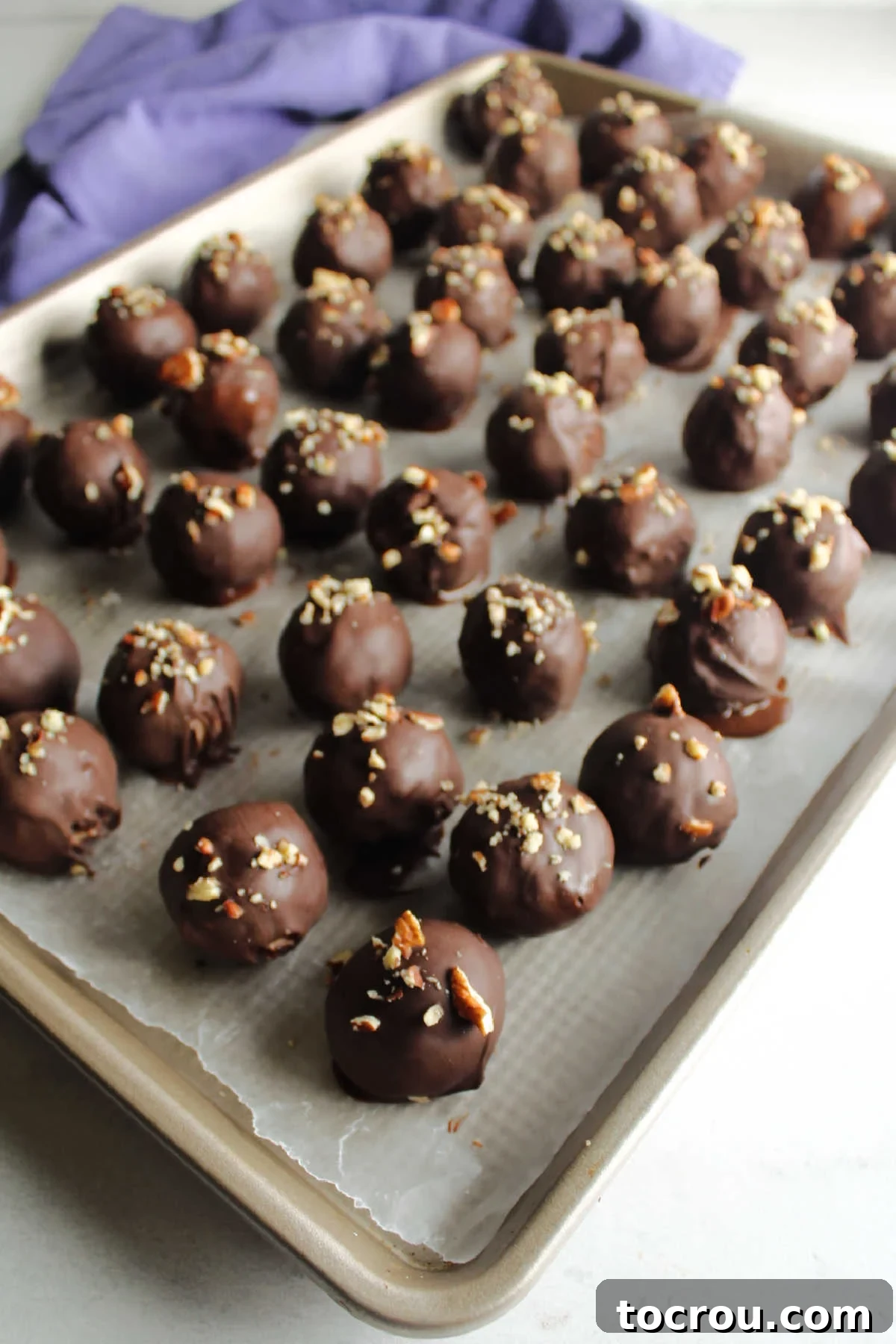 Chocolate coated coconut bon bons topped with bits of chopped pecans, setting up on wax paper lined tray.