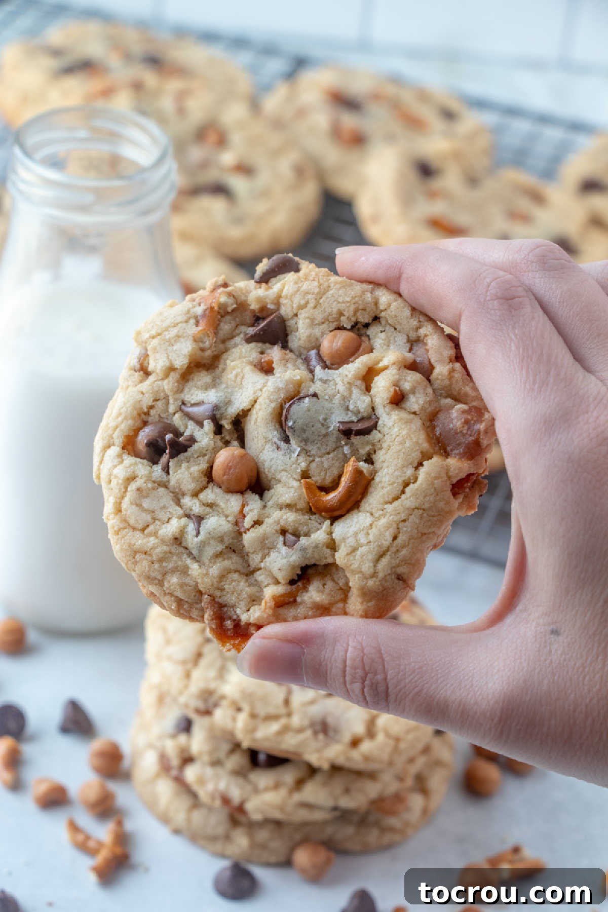 Hand holding a kitchen sink cookie with bits of pretzel, chocolate and caramel.