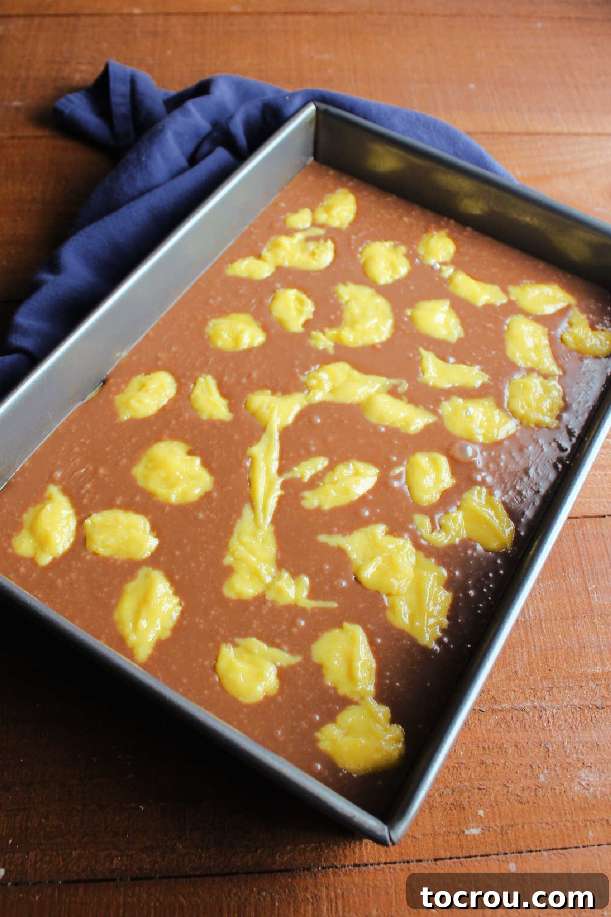 Fudge Bars Ready for the Oven A baking pan with a golden cake mix crust topped with a layer of chocolate peanut butter fudge, dotted with small, evenly scattered dollops of the remaining cake mix batter, ready for baking.