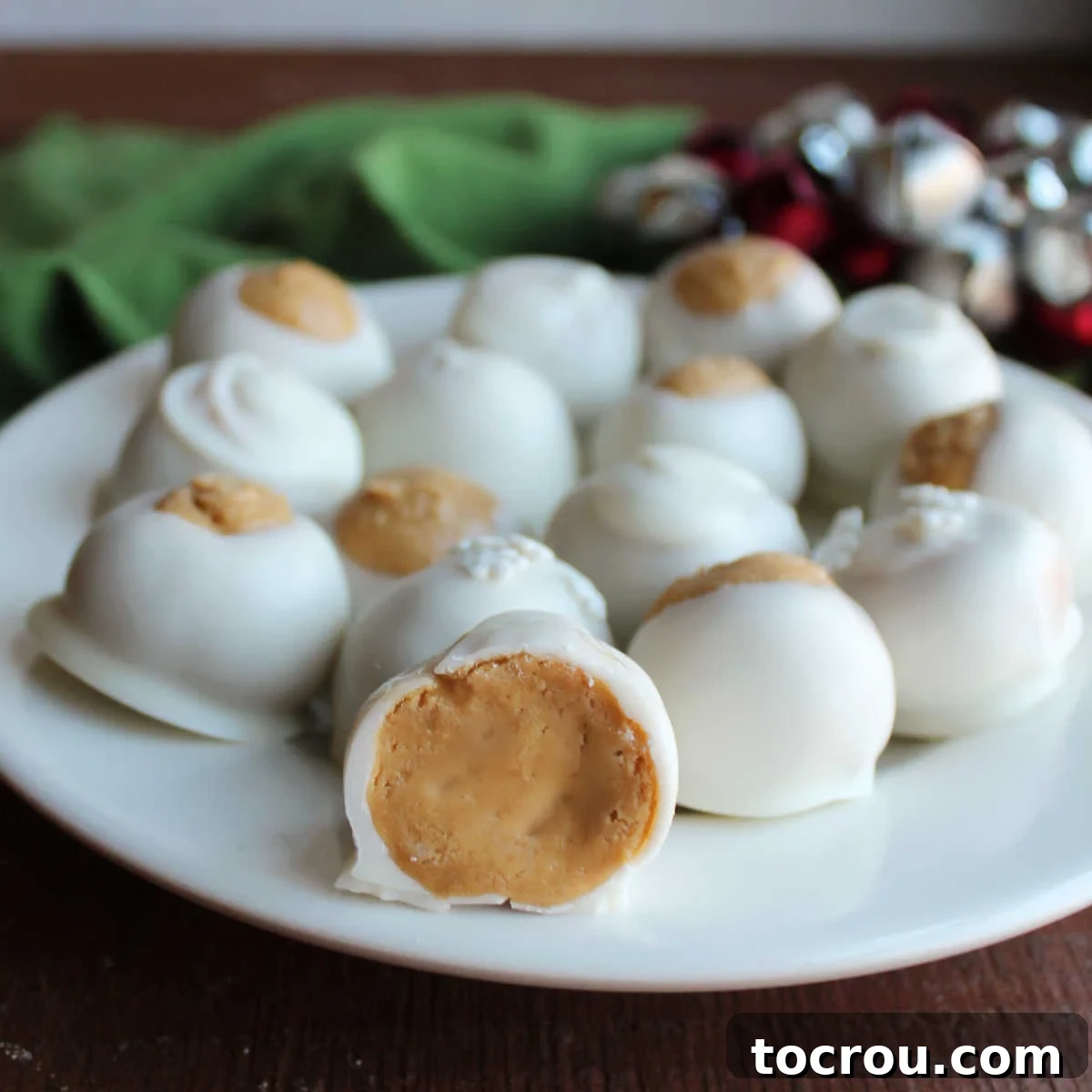 A beautiful plate featuring white chocolate dipped peanut butter snowballs and buckeyes, with one snowball sliced open to reveal its creamy peanut butter interior nestled within the crisp white chocolate shell.