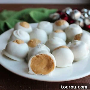 A inviting plate showcasing white chocolate dipped peanut butter snowballs and buckeyes, with one cut open to display the smooth peanut butter filling inside its white chocolate casing.