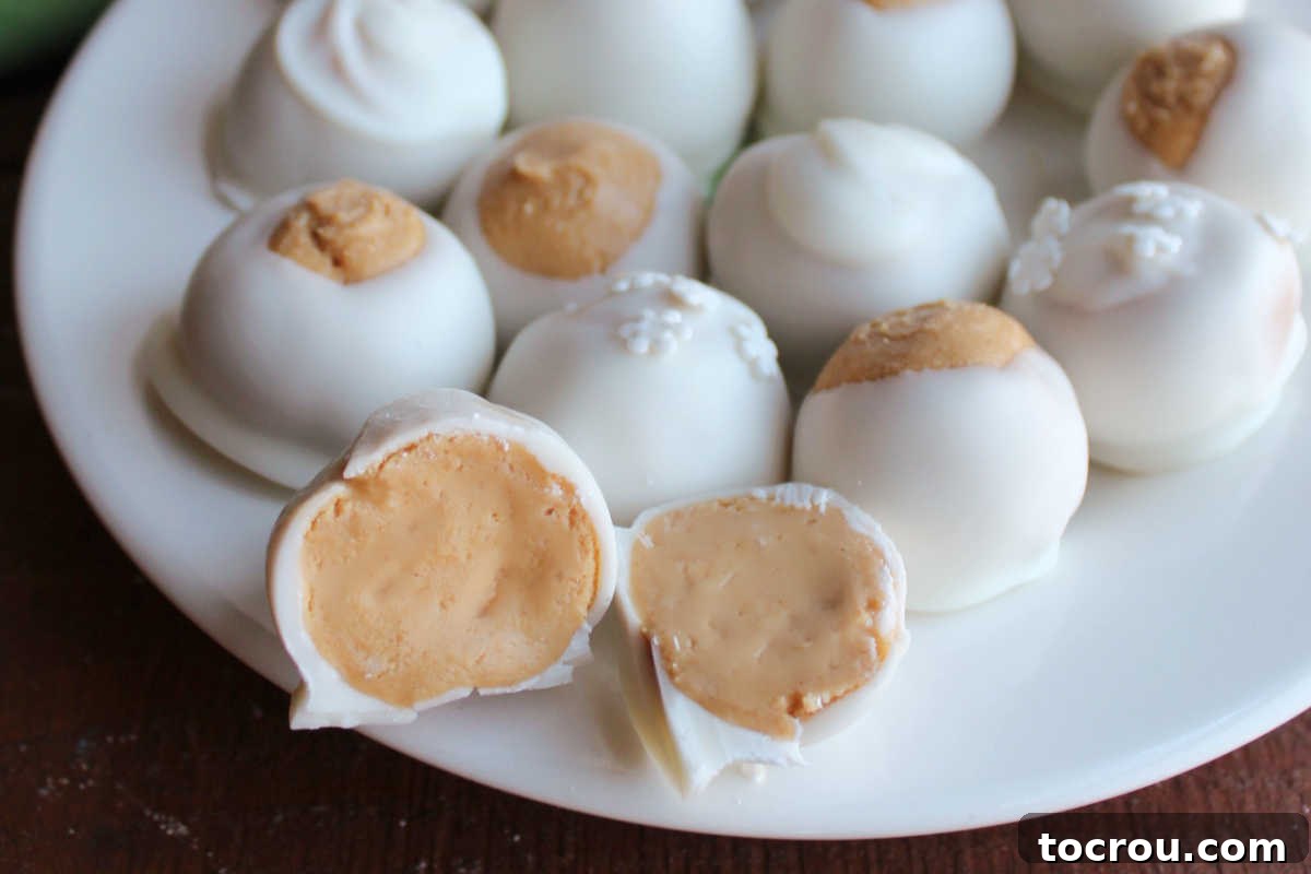 A close-up view of a perfectly cut peanut butter snowball, showcasing its smooth, light-colored peanut butter filling encased by a pristine white chocolate shell.