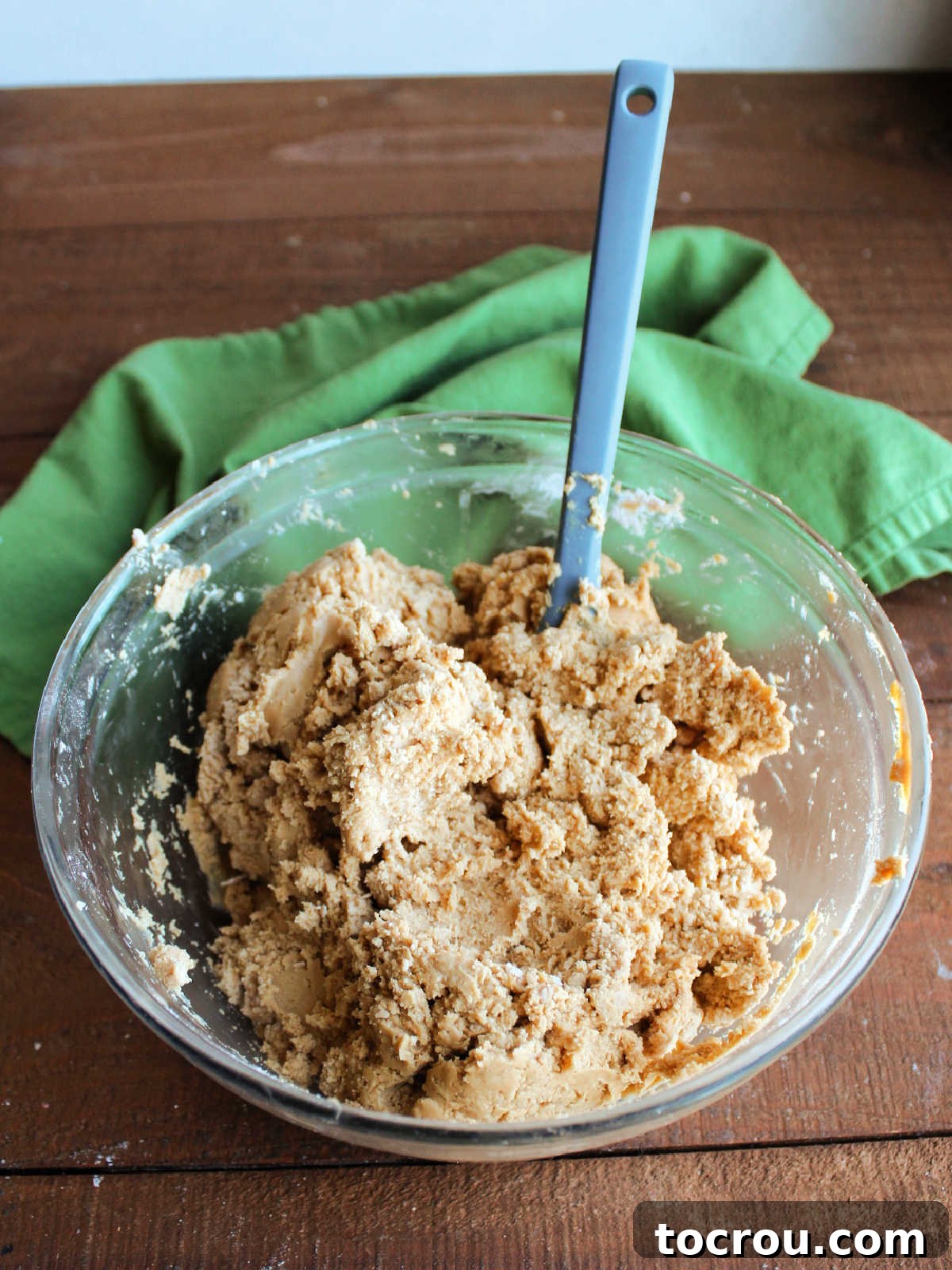 A bowl containing peanut butter filling, partially smoothed with a spatula, indicating it's starting to come together from its initial crumbly state.