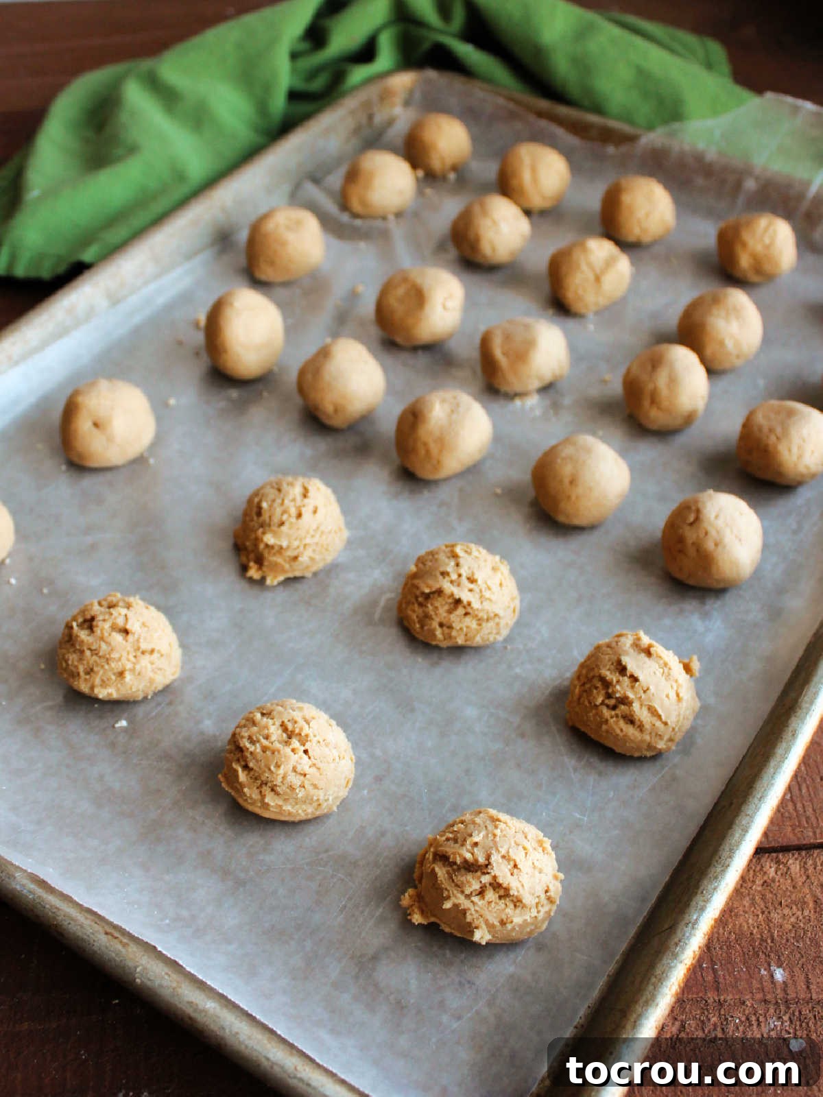 A baking tray lined with wax paper, holding scoops of peanut butter filling. Some scoops are still jagged from the scooper, while others are smoothed into perfect balls after being rolled.