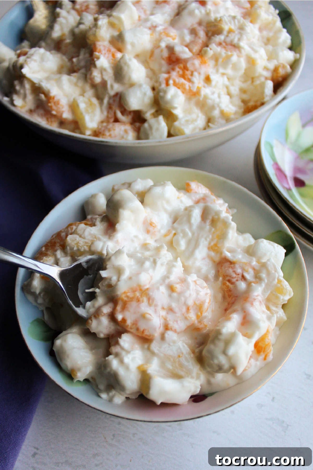 Spoon with a bite of five cup salad over a small bowl of served five cup salad showing fruit coated in creamy sour cream dressing.