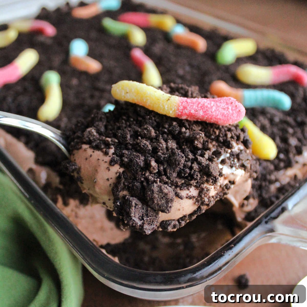 Serving spoon filled with dirt cake showing layers of Oreo crumbs, fluffy chocolate pudding mixture and sour gummy worms.