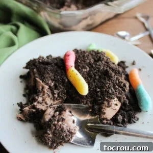 Close serving of chocolate dirt cake showing fluffy chocolate pudding and cream cheese filling with plenty of Oreo crumbs and gummy worms.