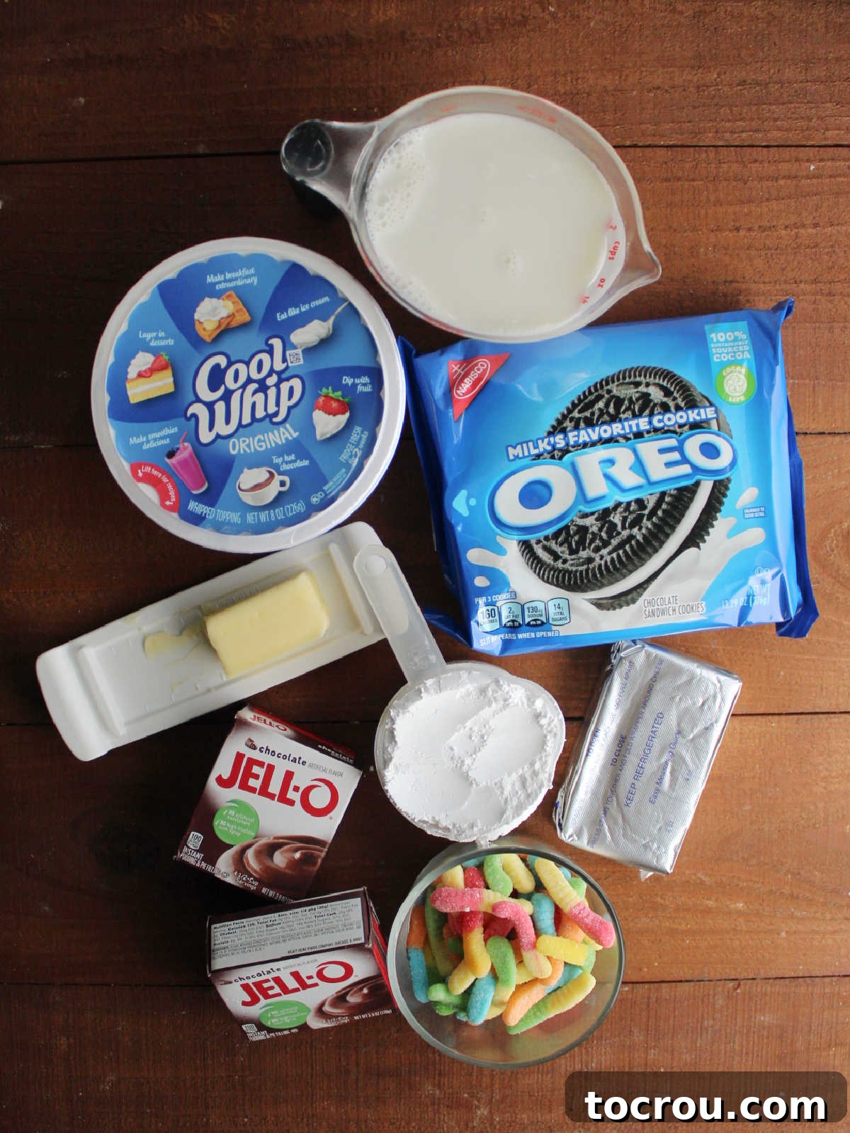 Dirt cake ingredients including Oreos, milk, chocolate pudding mix, butter, powdered sugar, cream cheese, Cool Whip and gummy worms.