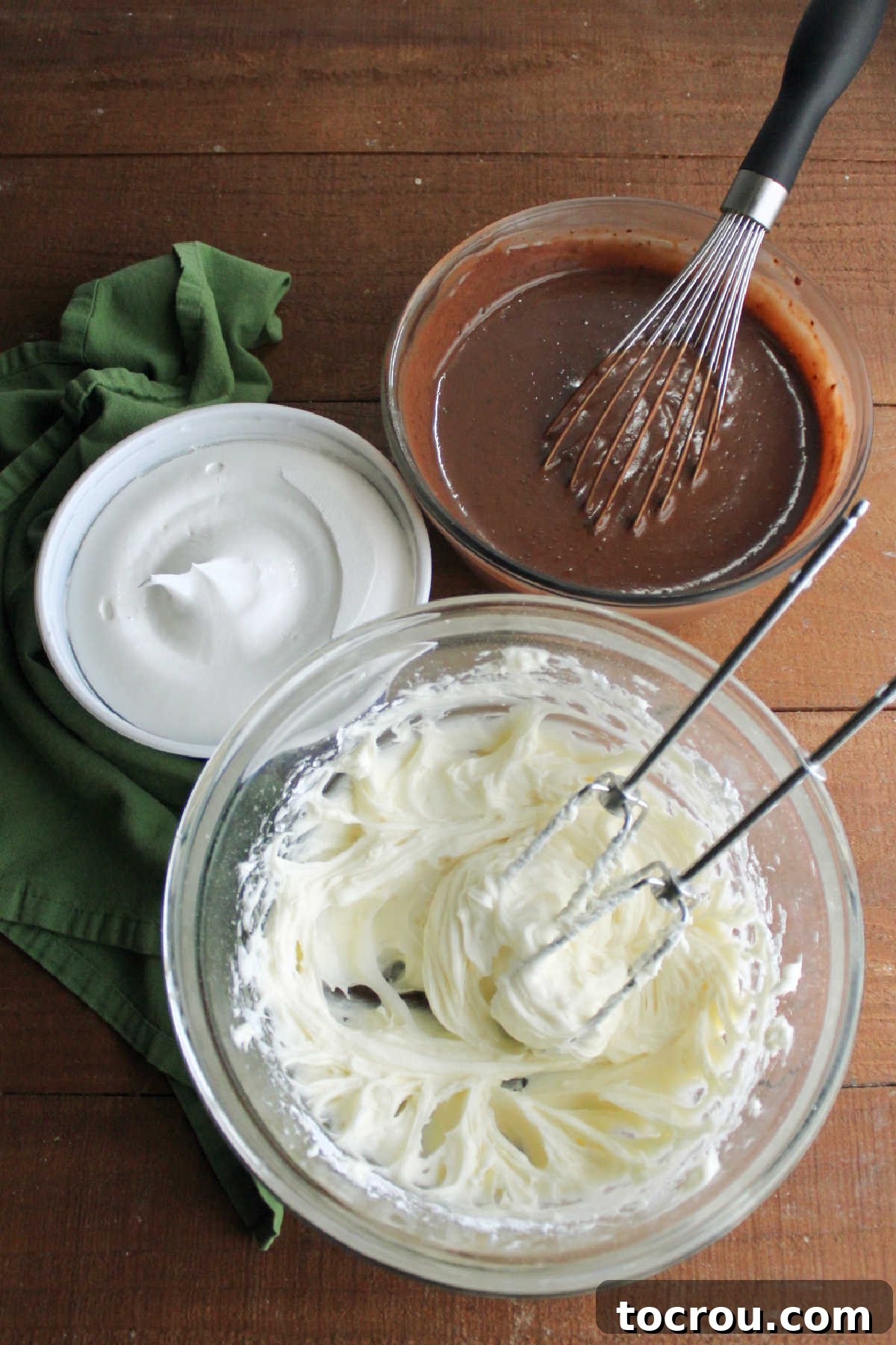 Mixing bowl filled with cream cheese, butter and powdered sugar mixture next to smaller mixing bowl with chocolate pudding and tub of cool whip ready to be combined to make the chocolate pudding filling.