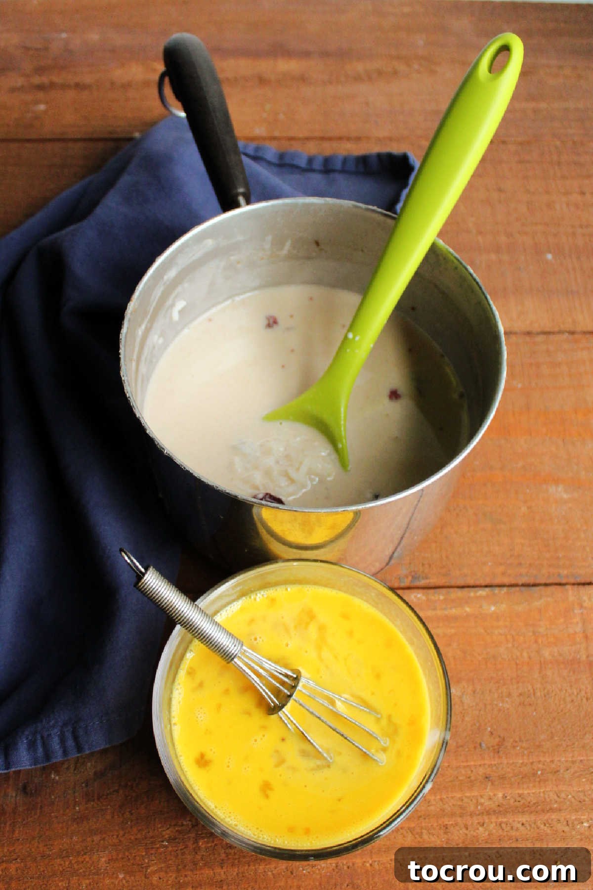 Tempering Eggs for Pudding Bowl of beaten eggs being tempered with the hot rice pudding mixture next to the saucepan with the remaining rice pudding mixture.