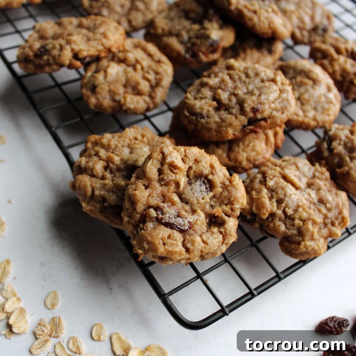 Delicious Oatmeal Cinnamon Drop Cookies Freshly baked chewy oatmeal cinnamon drop cookies cooling on a wire rack, with raw oats and raisins scattered nearby.