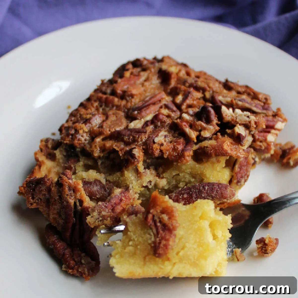 Bite of pecan pudding cake on fork showing dense texture of the cake layer topped with pecans and a crackly top.