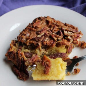 Bite of pecan pudding cake on fork showing dense texture of the cake layer topped with pecans and a crackly top.