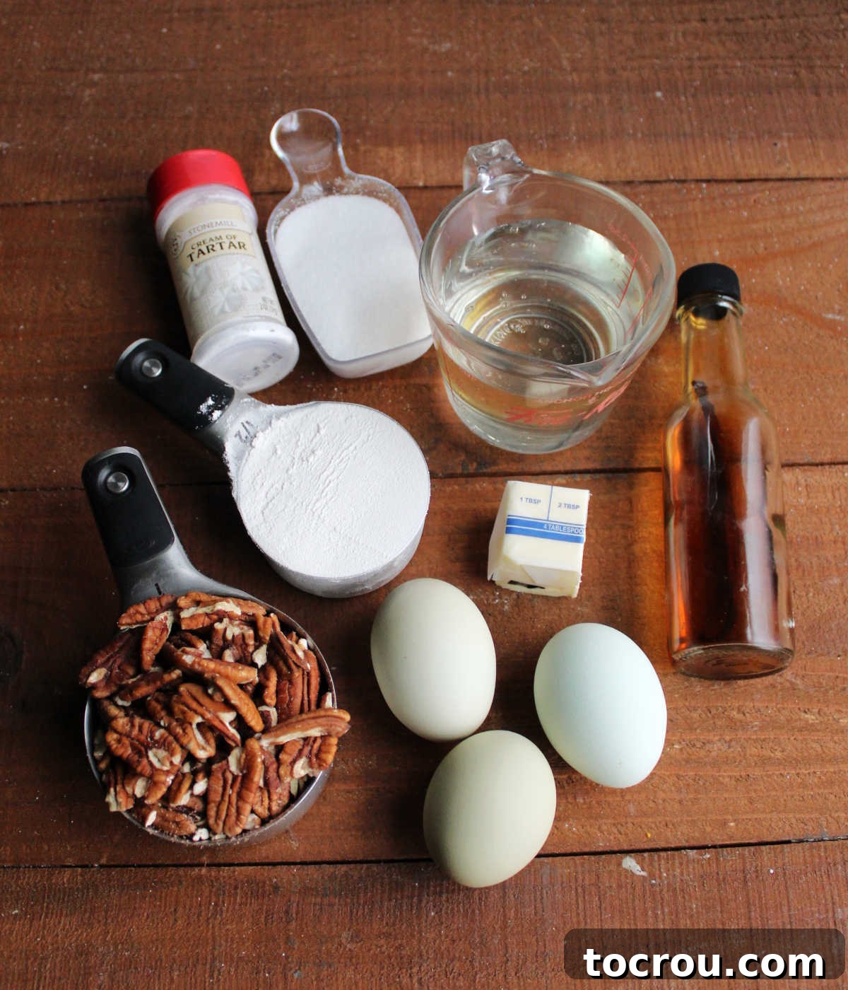 Ingredients including pecan, flour, eggs, sugar, corn syrup, butter, cream of tartar, and vanilla ready to be made into pecan pudding cake.
