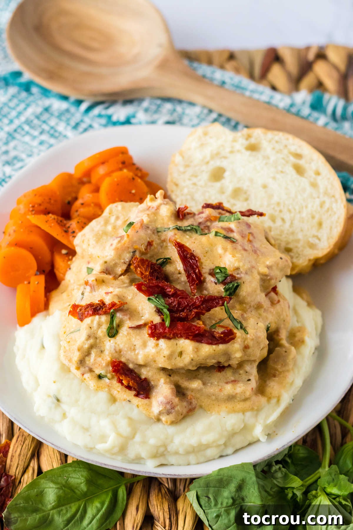 Dinner plate of slow cooker marry me pork chops garnished with extra sun dried tomatoes and basil served with mashed potatoes and carrots.