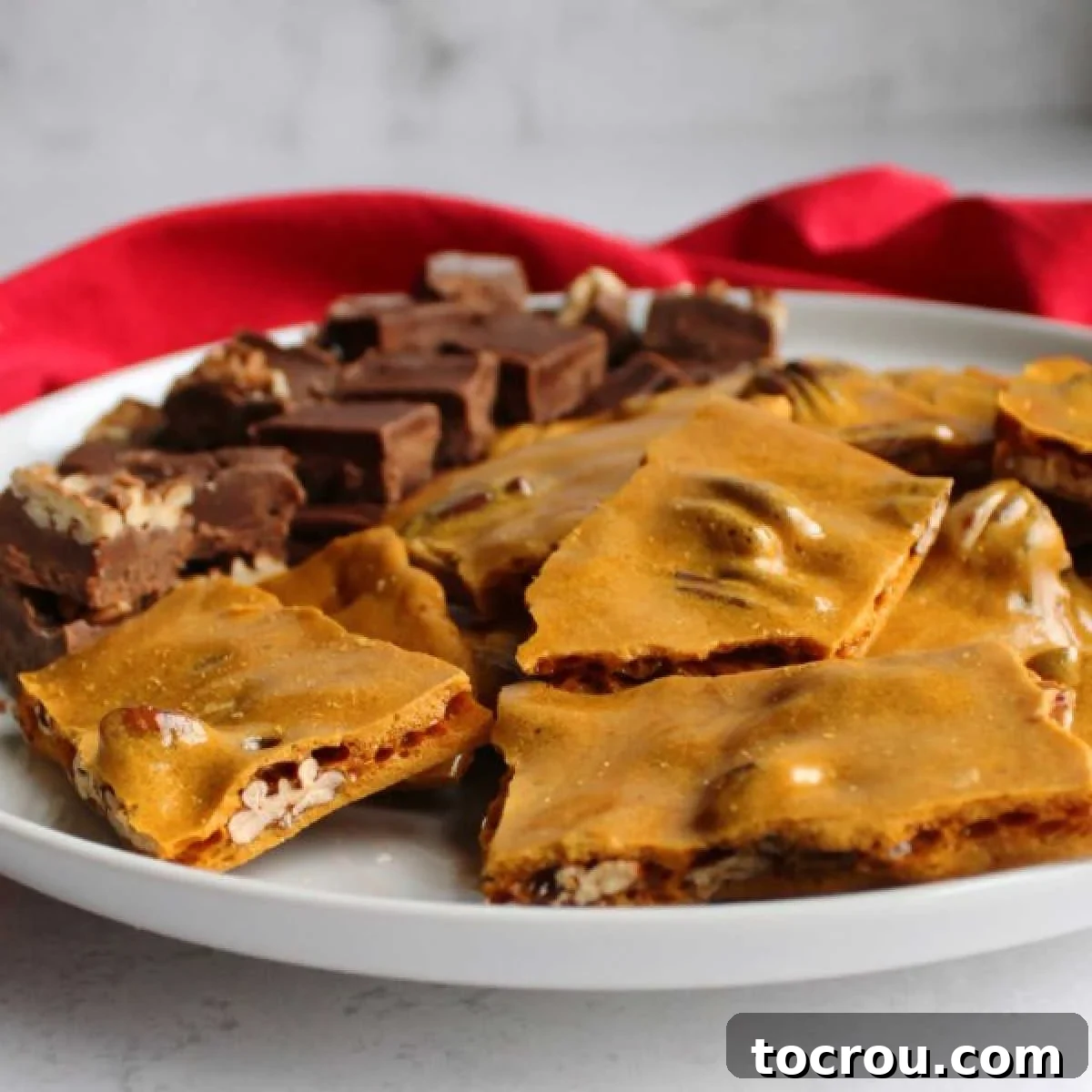 golden pecan brittle on plate with squares of fudge.