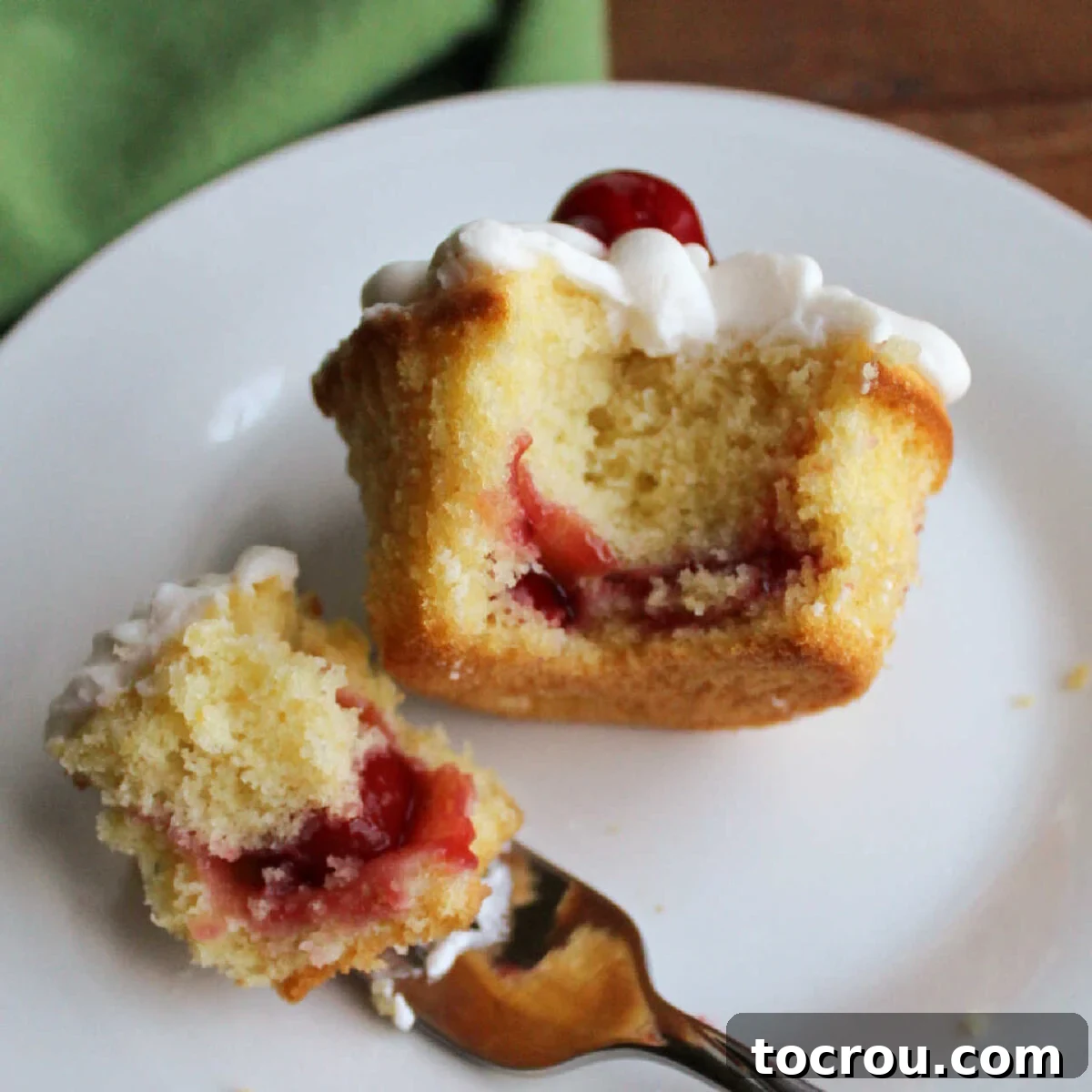 Cupcake on dessert plate with a bite on a fork showing moist crumb on the interior and cherry pie filling baked inside. 