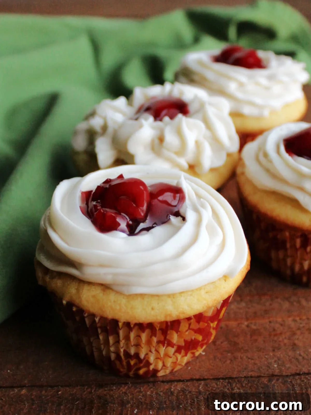Side view of vanilla cupcakes topped with a swirl of buttercream and cherry pie filling.