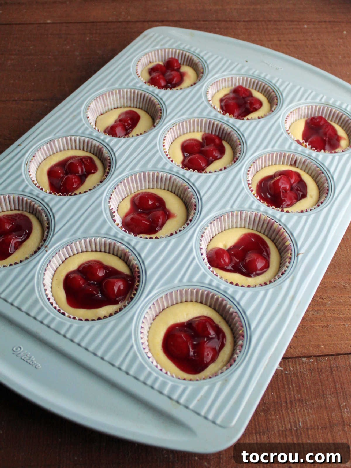 Cherry pie filling scooped on top of partially baked cupcake bases, ready for more cake batter.